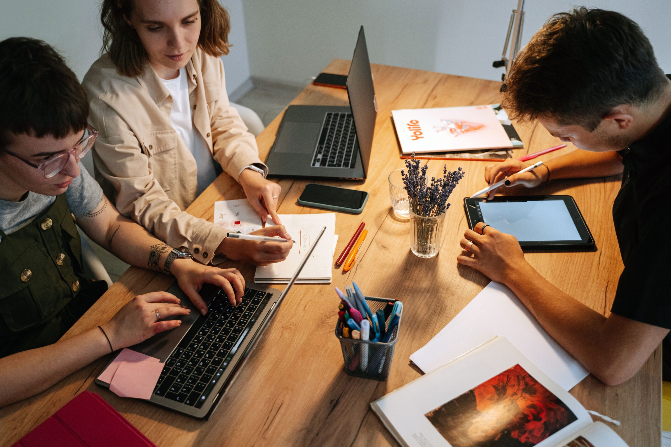 Three young professionals collaborating at a desk with laptops and tablets in a modern workspace.